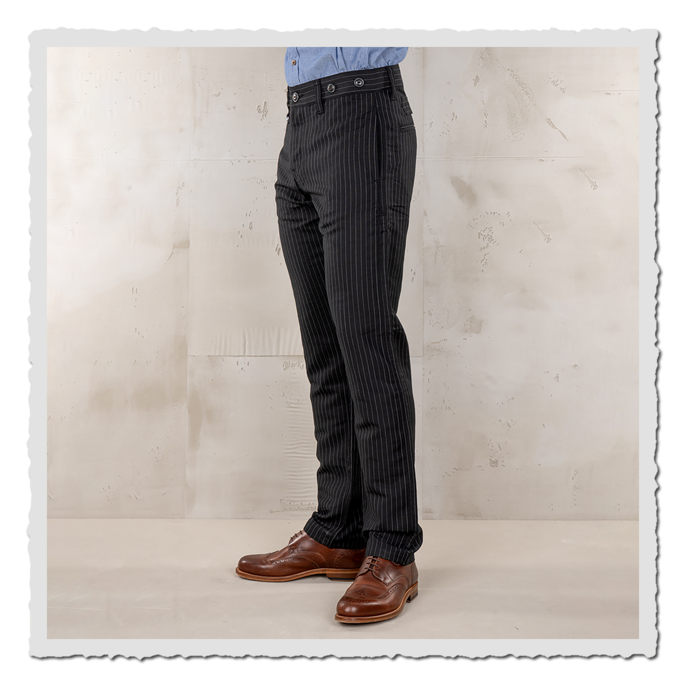 Schwarze Nadelstreifen-Hose am Model in Seitenansicht, von Bund bis Schuhe, hellgrauer Studiohintergrund.